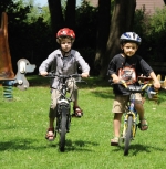 Zwei Kinder radeln nebeneinander mit Fahrradhelmen über eine Wiese
