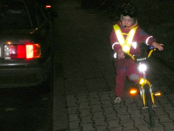Kleinkind mit reklektierender Kleidung auf einem Fahrrad neben einem Auto in der Dunkelheit