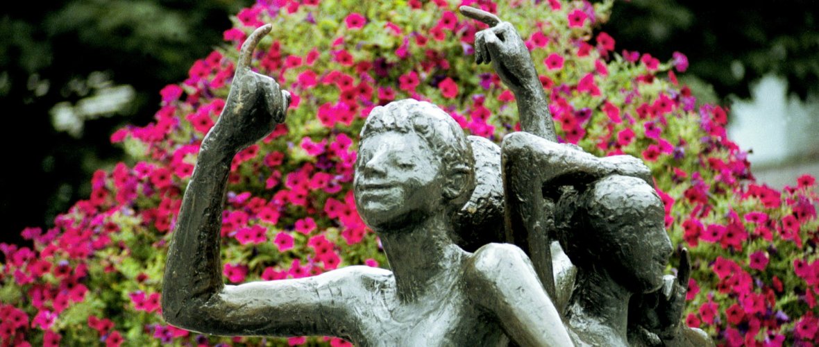 Klenke's monument. Three statues with raised little finger. Pink flowers in the background