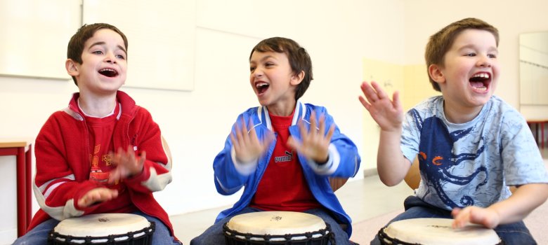 Three children drumming with their hands on djembes.