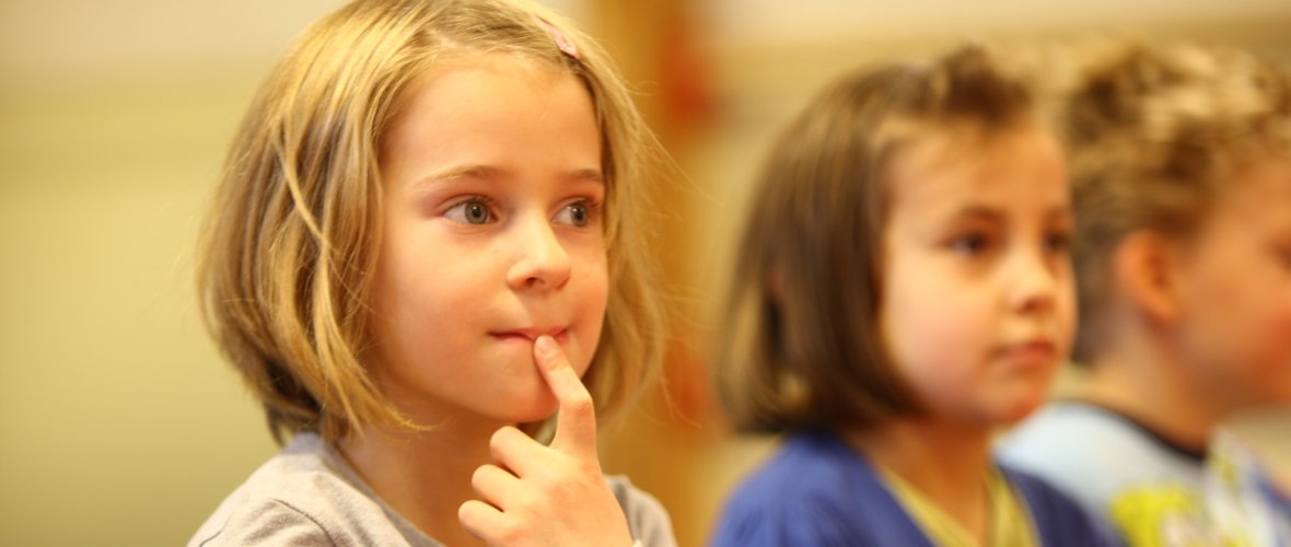 A girl holds a finger over her mouth and makes big eyes