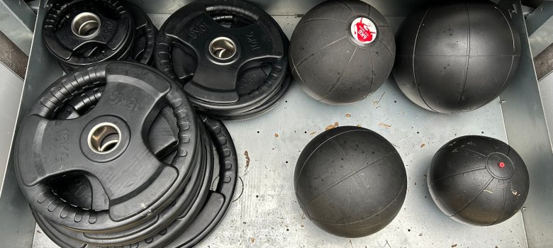 A drawer of the sports box with several pieces of equipment such as balls and weight plates.
