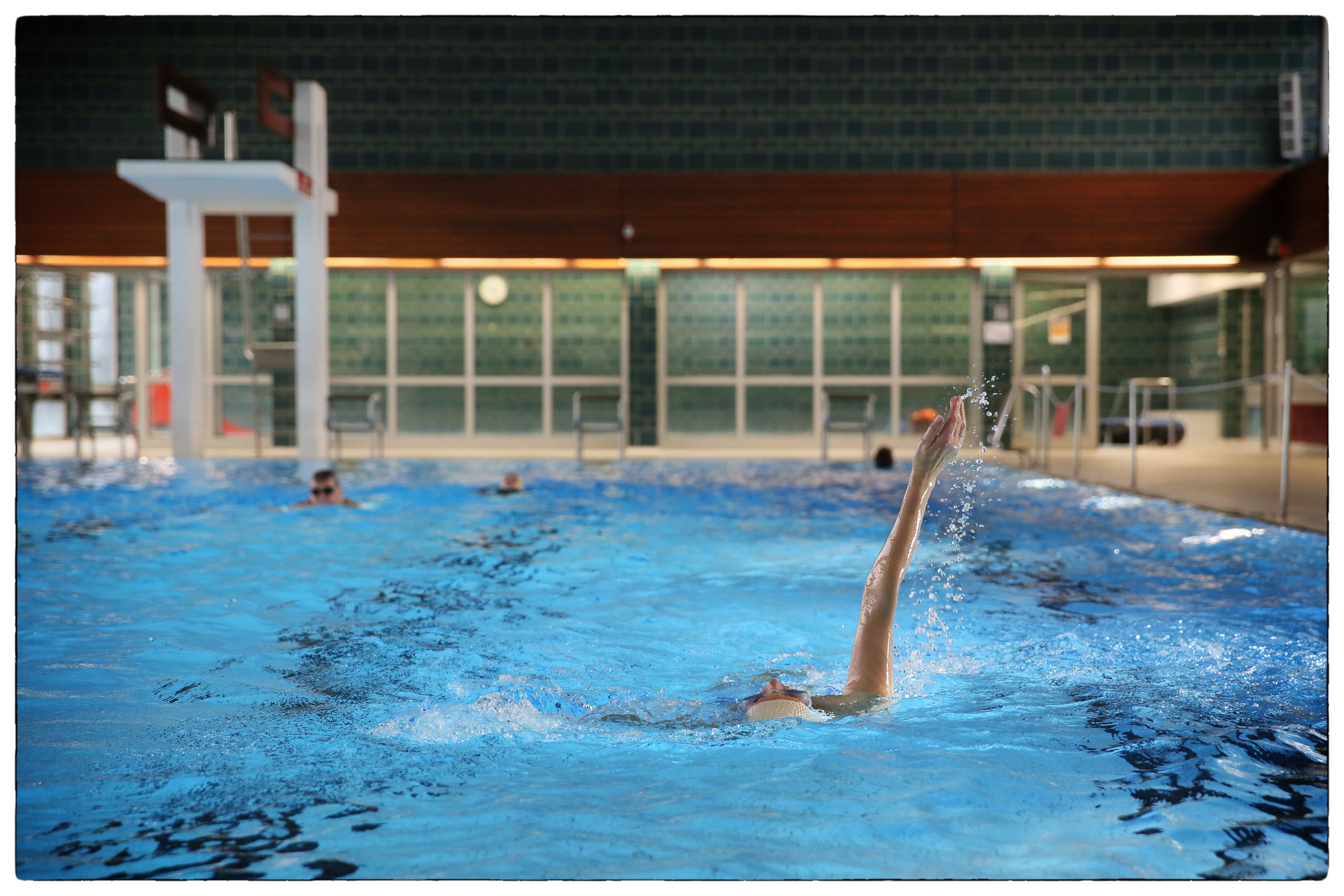 The water basin of the Brand indoor swimming pool A swimmer crawls on her back in the pool of the Brand indoor swimming pool. The diving tower can be seen in the background