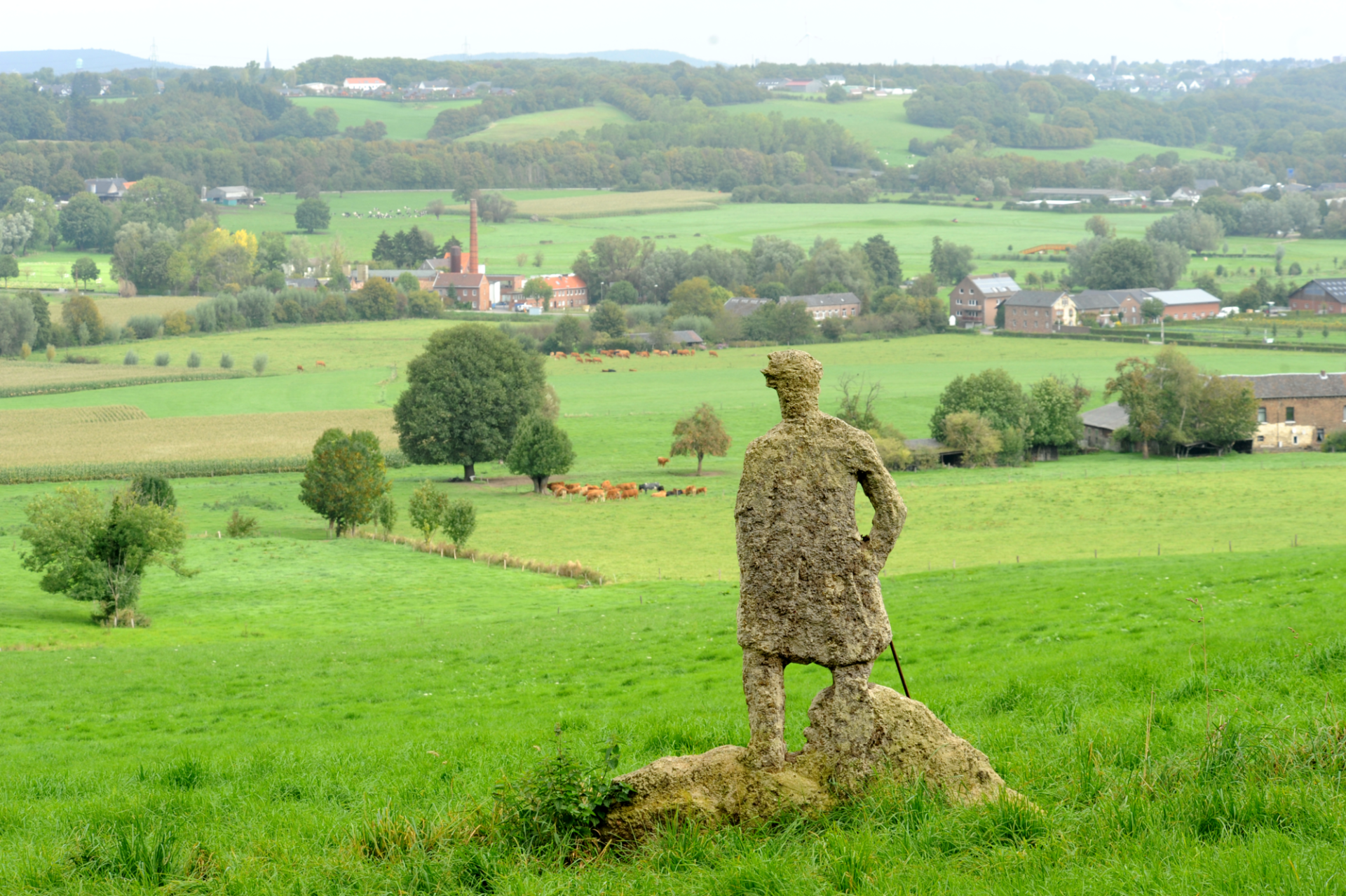 A green landscape in summer, with a bronze statue of Caspar David Friedrich's Wanderer in the foreground.
