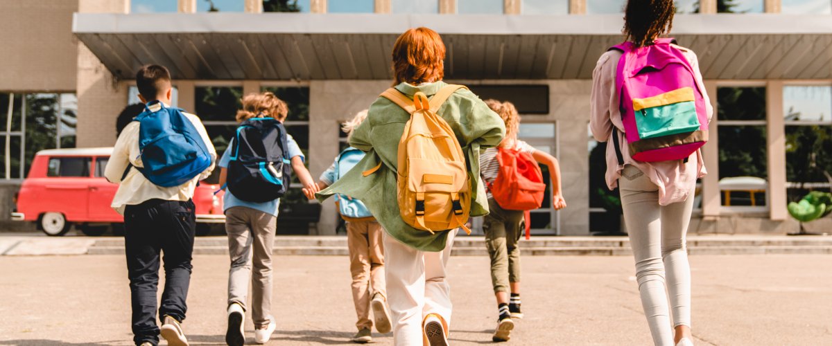 Group of schoolchildren running hurriedly to the school building .