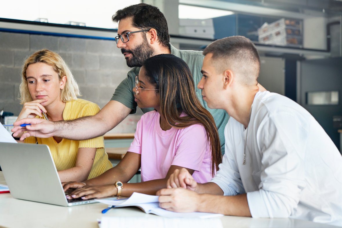 Young teacher helps teenagers on the computer.
