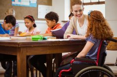 Inclusion Teacher helps a pupil in a wheelchair with other children at the table.