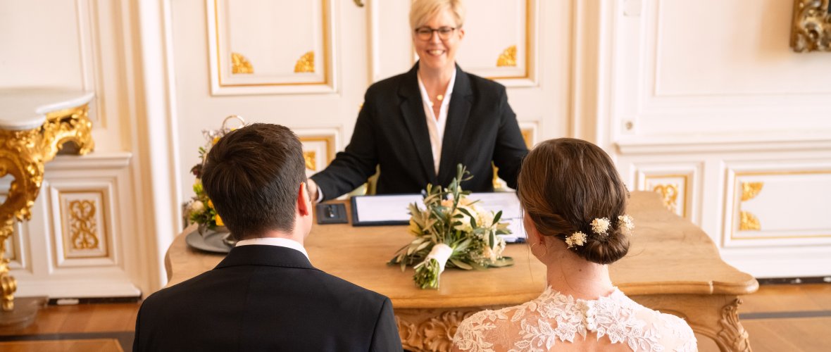 You look over the shoulders of the bride and groom to the smiling registrar