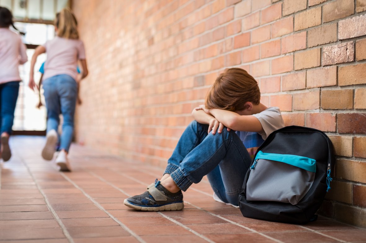 Sad schoolboy sitting in the corridor, hands on his knees and head between his legs.