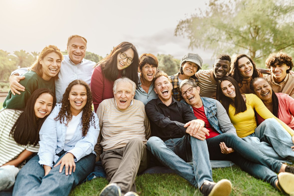 Happy group of people from different generations and nations sitting in the park and laughing into the camera