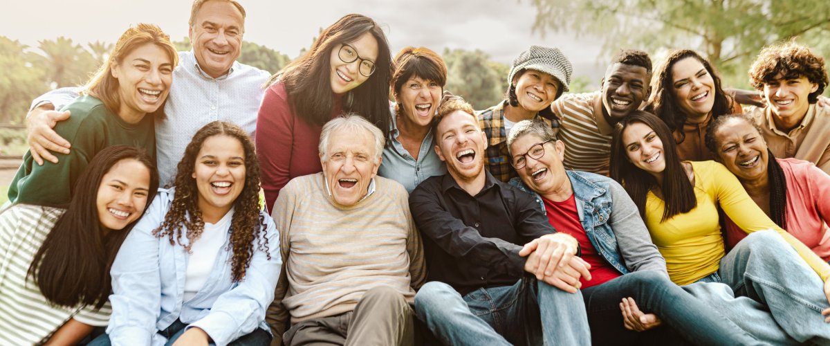 Society Happy group of people from different generations and nations sitting in the park and laughing into the camera