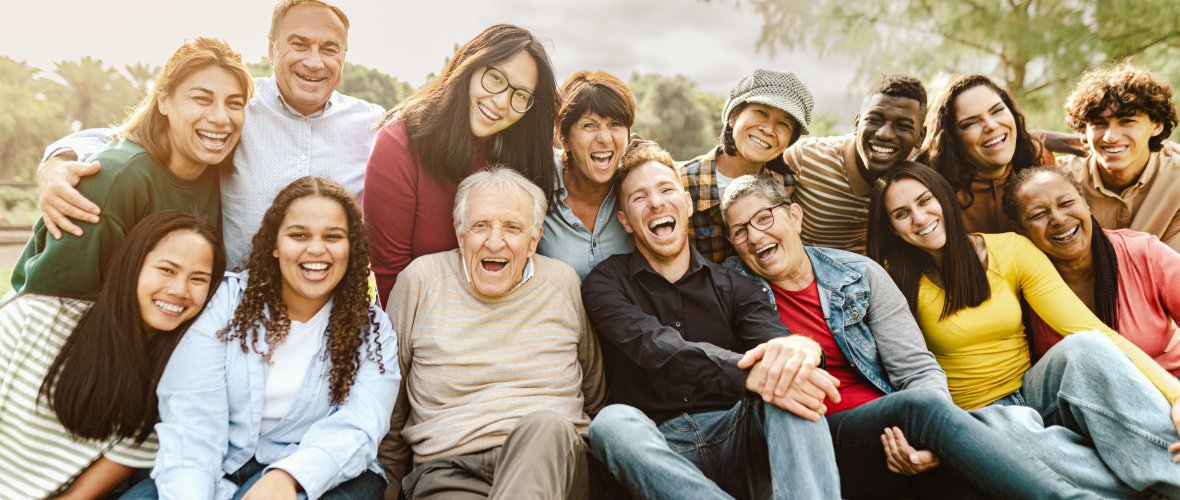 Happy group of people from different generations and nations sitting in the park and laughing into the camera