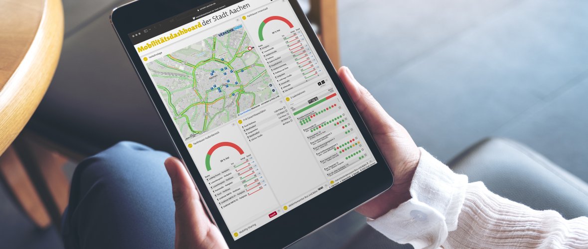 Woman sitting cross-legged, holding a tablet with the city of Aachen's mobility dashboard.