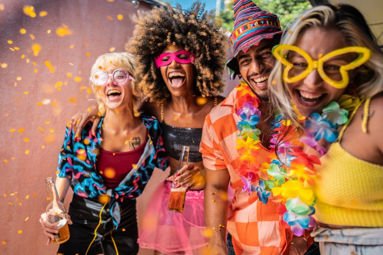 Four people in colorful costumes celebrate carnival together and laugh into the camera.