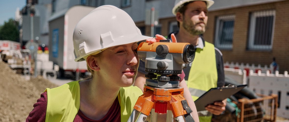 Apprentice with construction site clothing and helmet looks through a measuring device