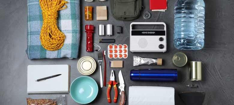 Disaster supply kit with various items laid out on dark gray table.