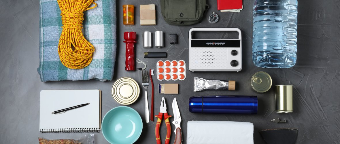 Disaster supply kit with various items laid out on dark gray table.