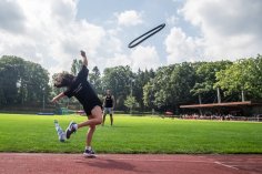 Competition in the forest stadium A girl in sportswear is doing a ring toss in the forest stadium. A man looks on.
