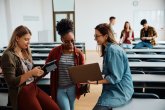 Study Female students stand relaxed with laptop and tablet in a lecture hall.
