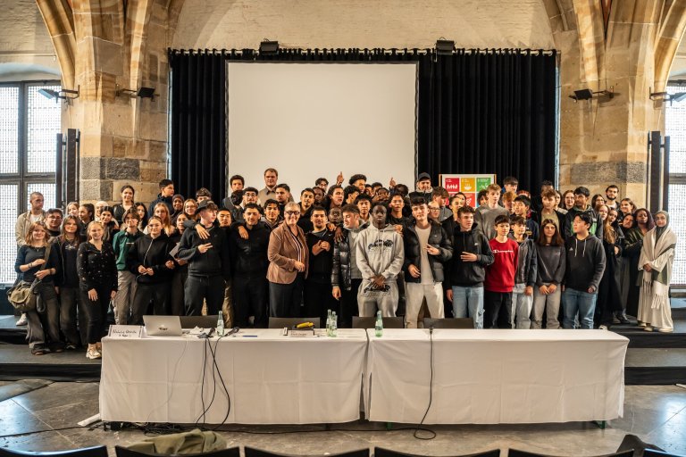 Mayor Sibylle Keupen stands in the middle of many laughing young people on the stage in the Coronation Hall of the Town Hall.