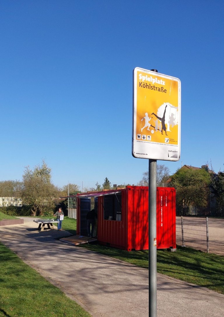Ein roter Container steht auf einem Spielplatz, im Vordergrund ein Schild mit der Aufschrift "Speilplatz Köhlstraße"