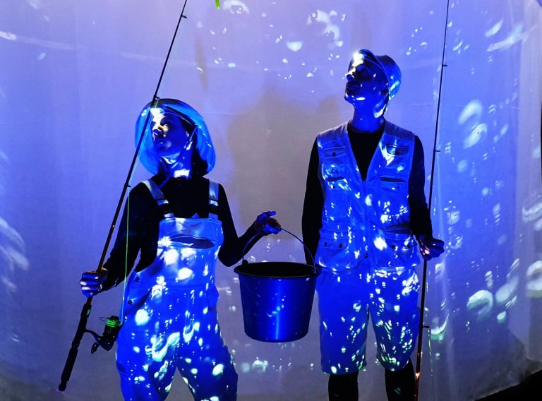Two people in fishing costumes stand in the blue light.