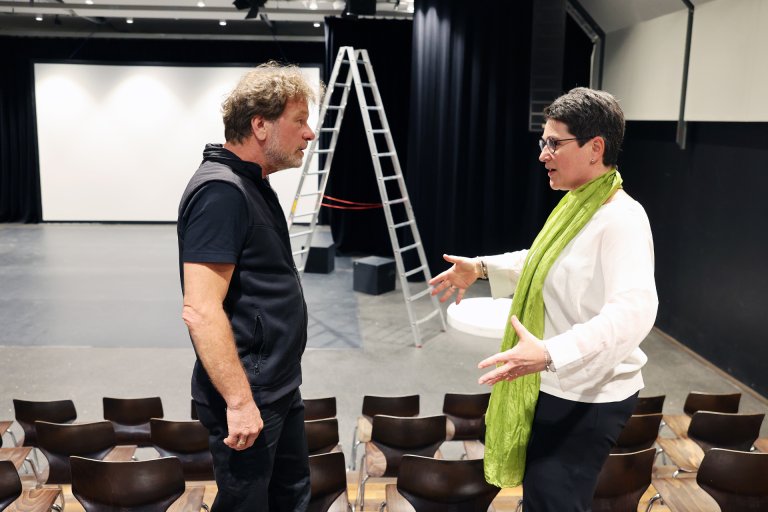 Two people talking to each other. A stage area in the background