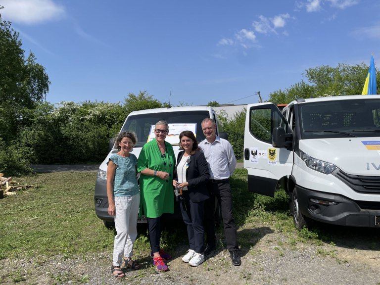 Four people are standing in front of two vehicles.