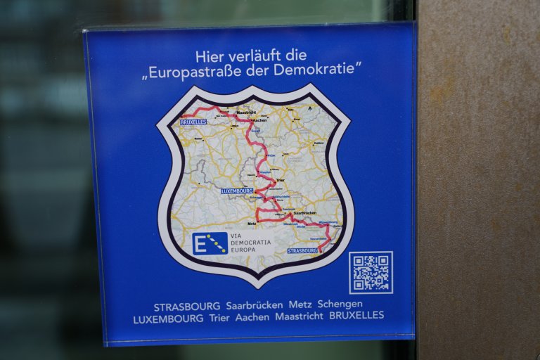 A blue plaque with a map showing the route between Strasbourg and Brussels. Above it is the inscription: This is where the "European Route of Democracy" runs.