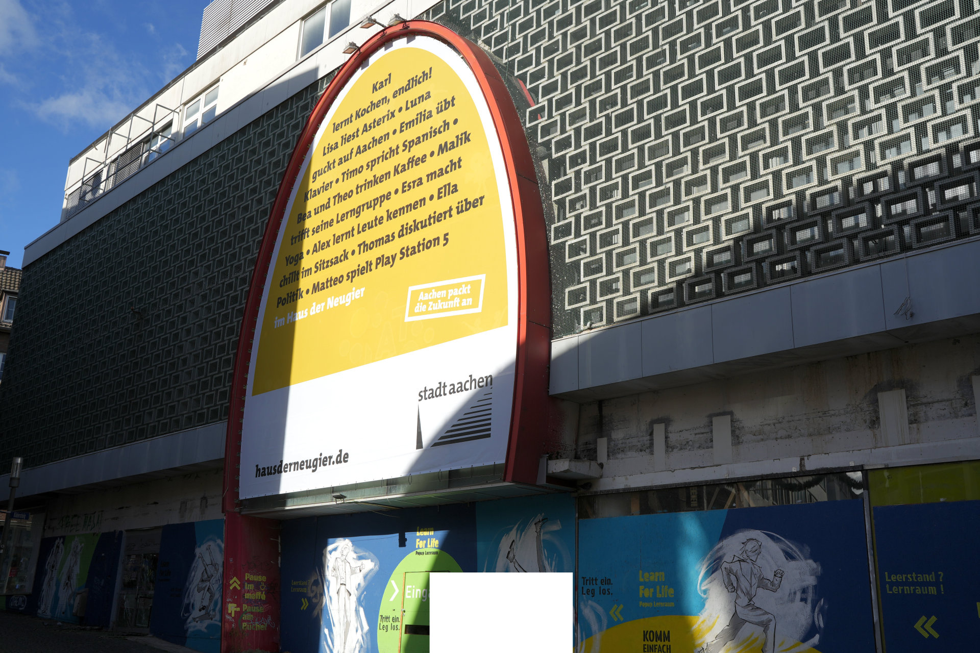 A large oval banner can be seen hanging on the façade of a former department store. The banner is an example of what can be done in the House of Curiosity in the future.
