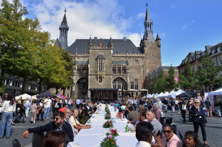 A long table of 30 meters on a square, surrounded by people, with Aachen City Hall in the background