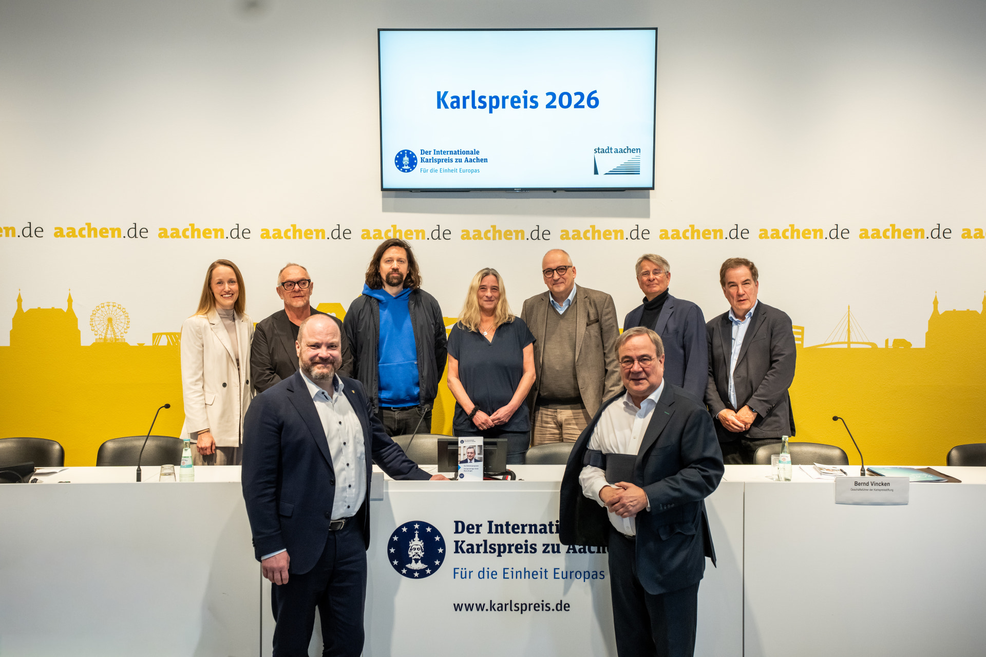 A group of people stand in front of a yellow and white background with the Charlemagne Prize logo.