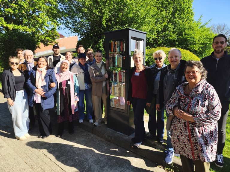 A group of people placed to the left and right of a bookcase in the sunshine.