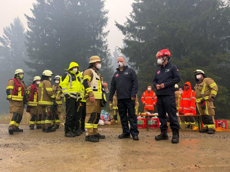 Several firefighters and Mayor Michael Ziemons are standing in a wooded area in the High Fens.