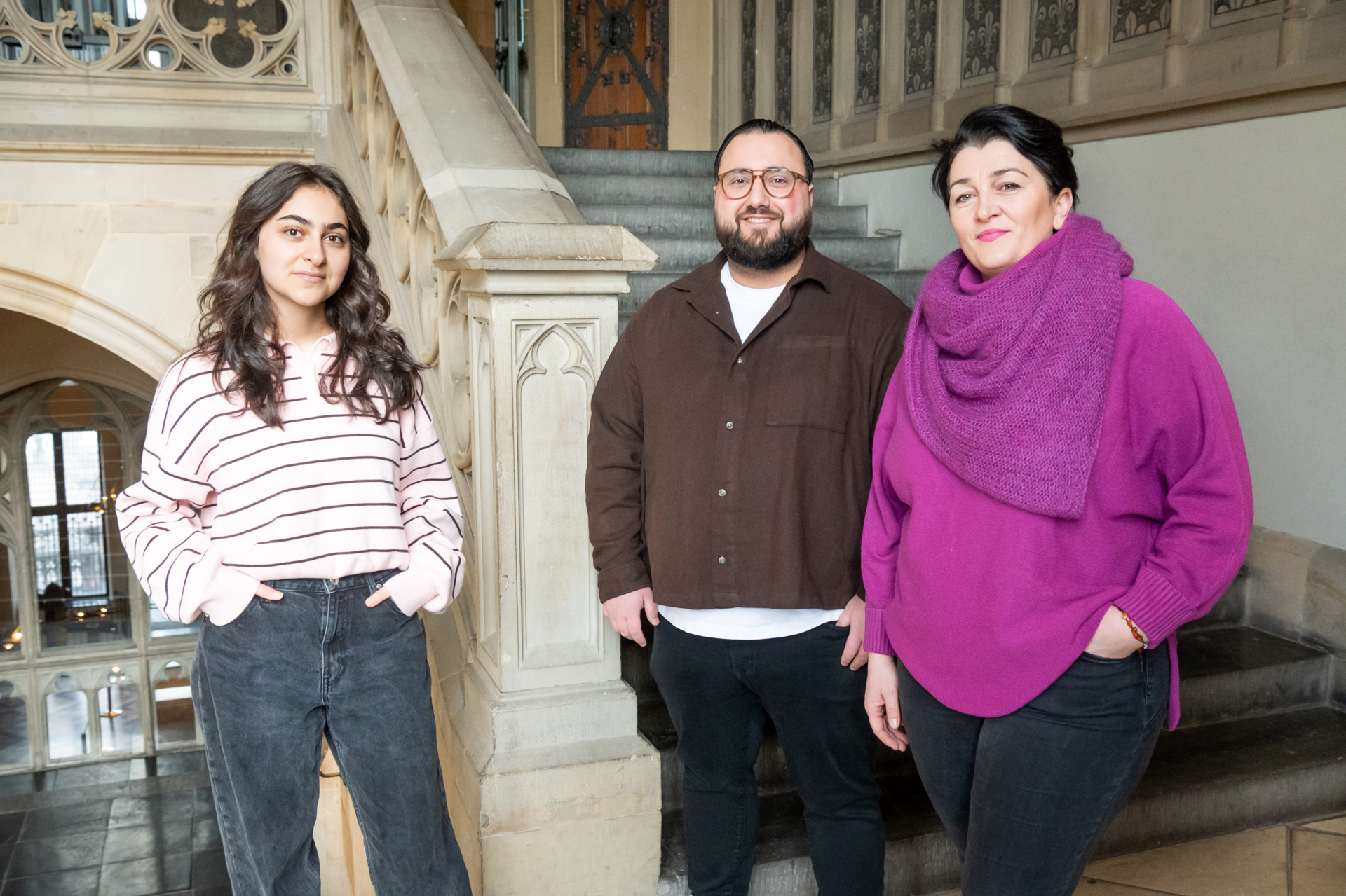 Three people, a woman on the left, a man in the middle and a woman on the right, stand in the stairwell of Aachen City Hall.