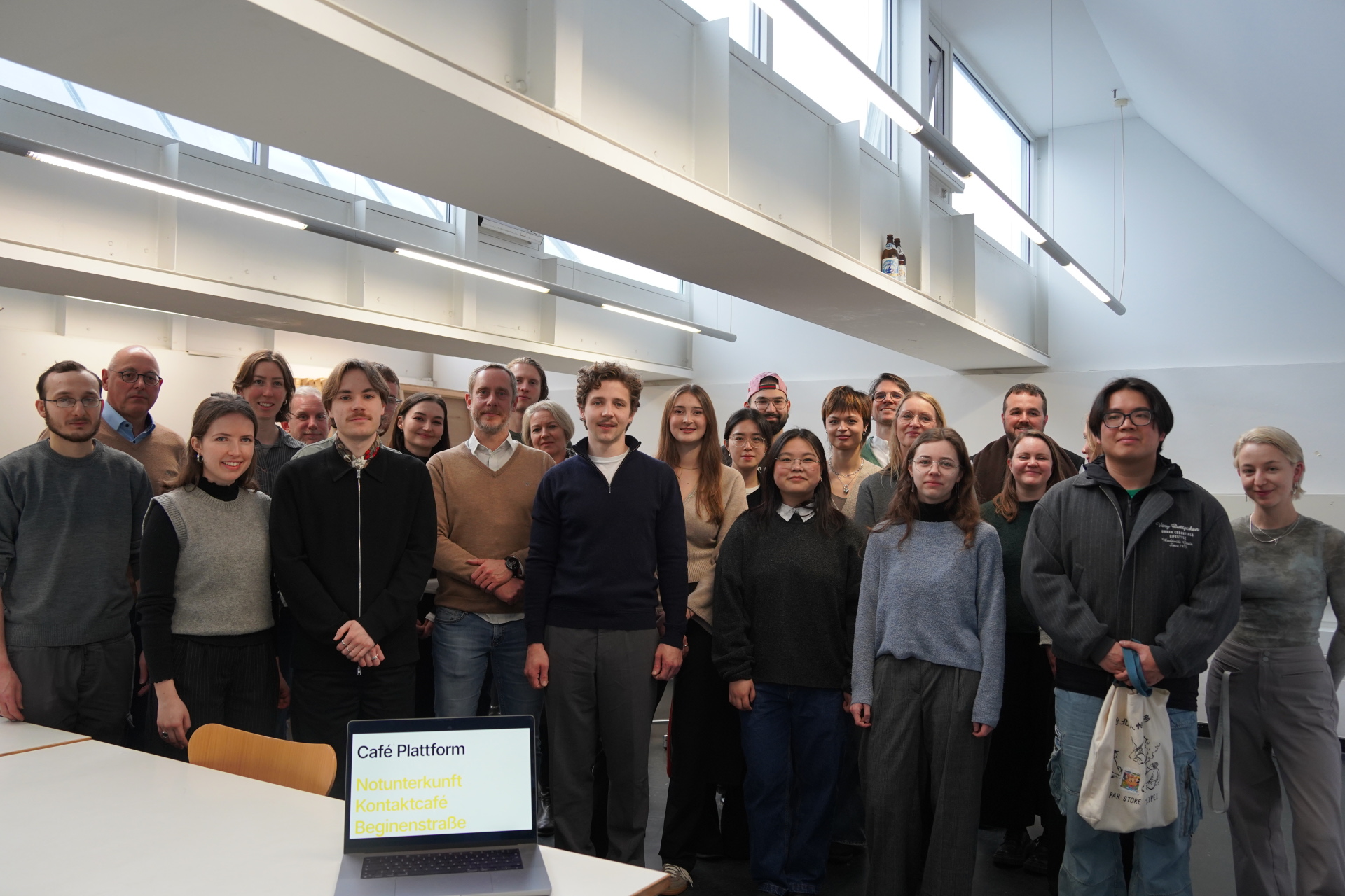 A large group of people are standing in a white room in front of a table with a laptop.