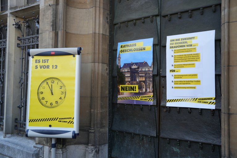 Two posters are hanging on the town hall door, and in front of them is another poster attached to a flip chart outside the door.