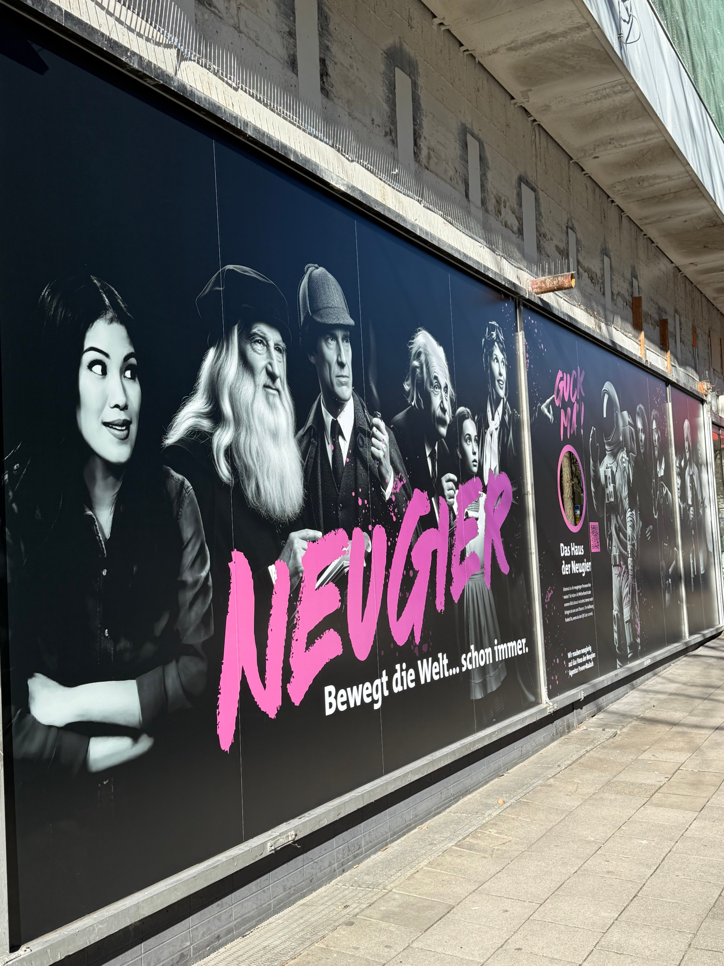 A window display with pink lettering "Curiosity" and people from real and fictional history on a black background