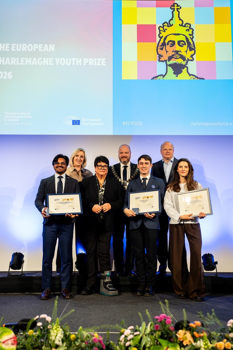 Three young people hold certificates up to the camera with four other people standing next to them.