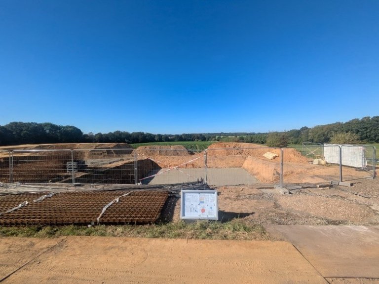 A freshly poured concrete slab in the middle of a construction site. Meadows and trees in the background.