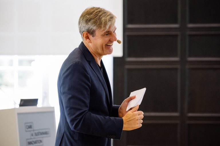 A man wearing a headset smiles and speaks to an audience