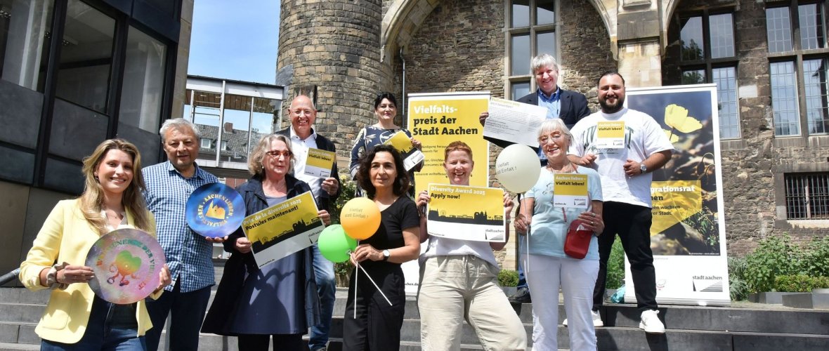 Conseil d'intégration Au total, dix personnes du conseil d'intégration et de l'administration se tiennent sur les marches du Katschhof d'Aix-la-Chapelle, tenant dans leurs mains des documents d'information sur le thème de la diversité et de la remise des prix.