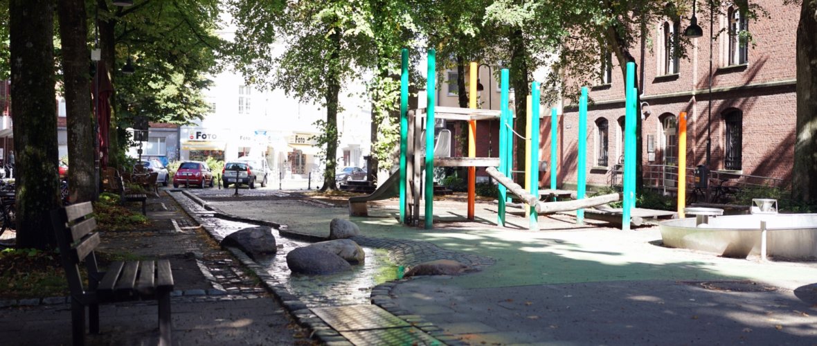 La Lindenplatz à Aix-la-Chapelle, avec un ruisseau à ciel ouvert et une aire de jeux dotée d'une structure d'escalade en arrière-plan.