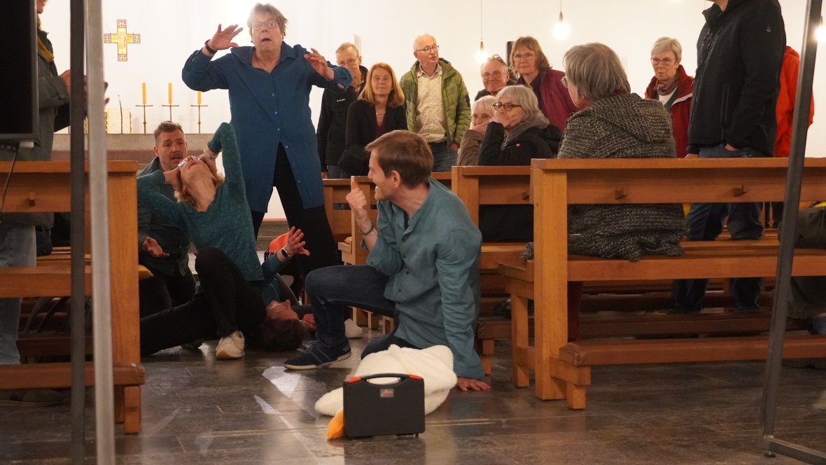 Des acteurs présentent une pièce de théâtre improvisée dans l'église. On les voit essayer d'atteindre une valise pleine d'argent au ralenti.