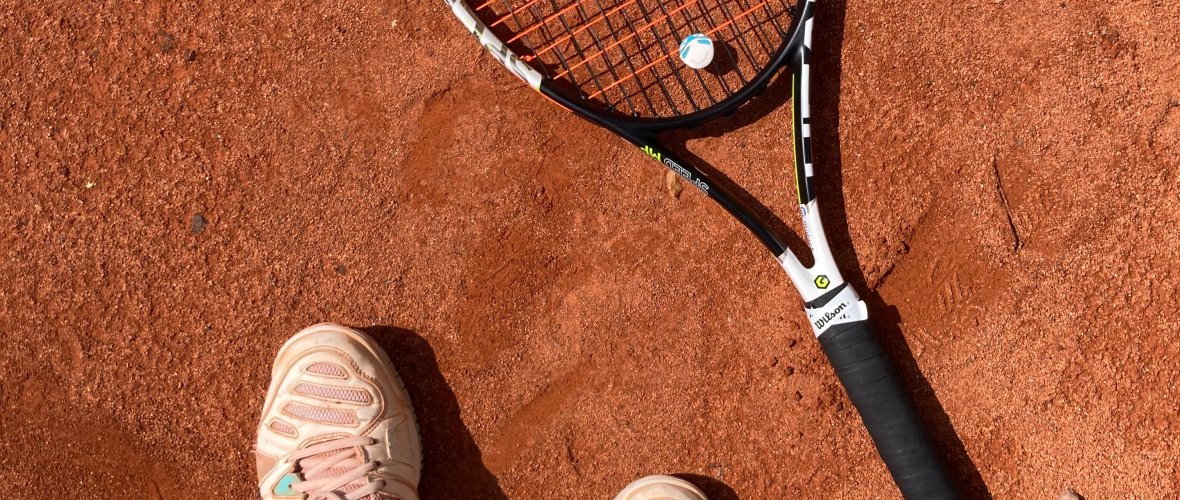 Une raquette de tennis est posée à côté d'une paire de pieds sur le terrain en cendres.