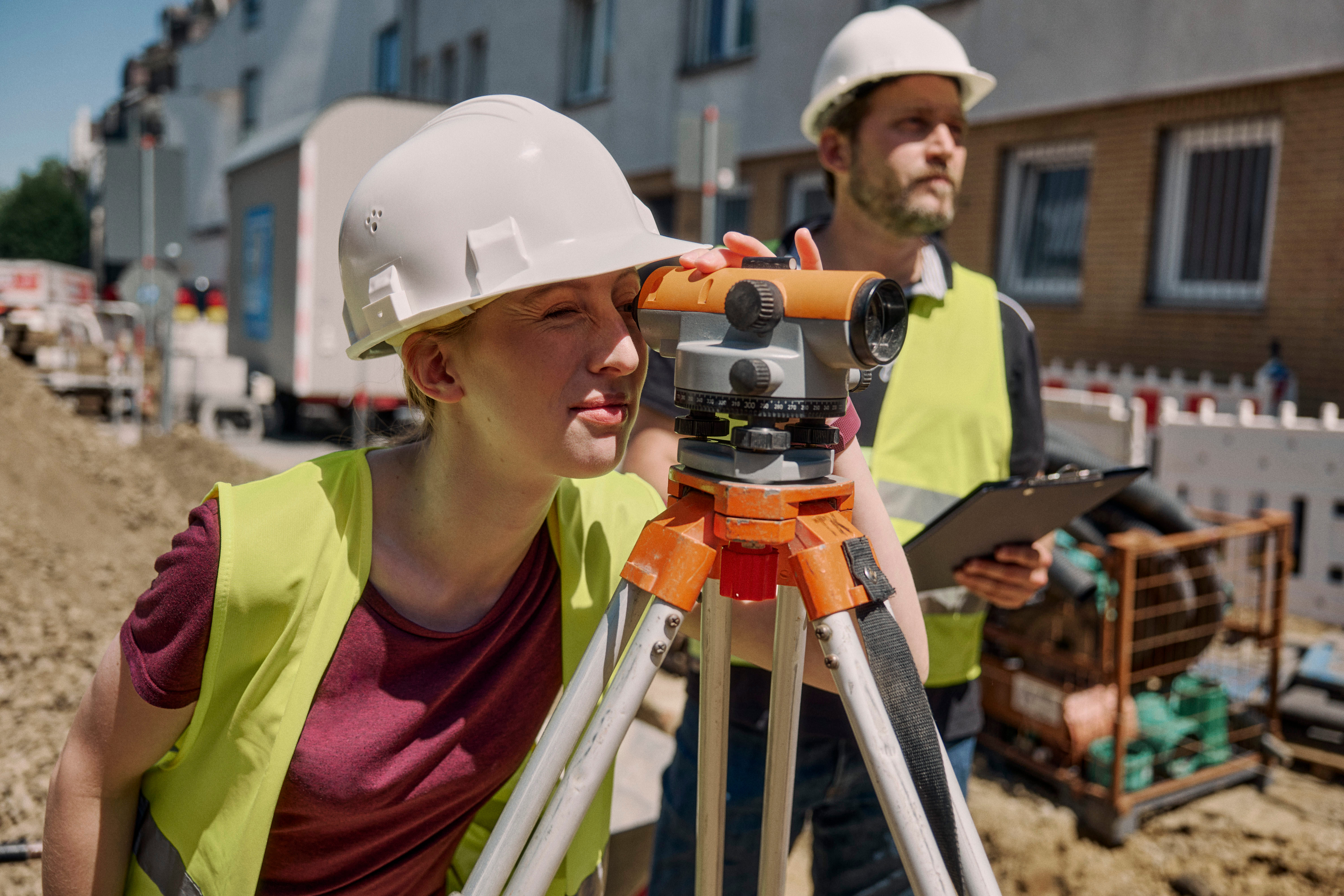 Construire & planifier Apprentie en tenue de chantier et casque regardant à travers un appareil de mesure