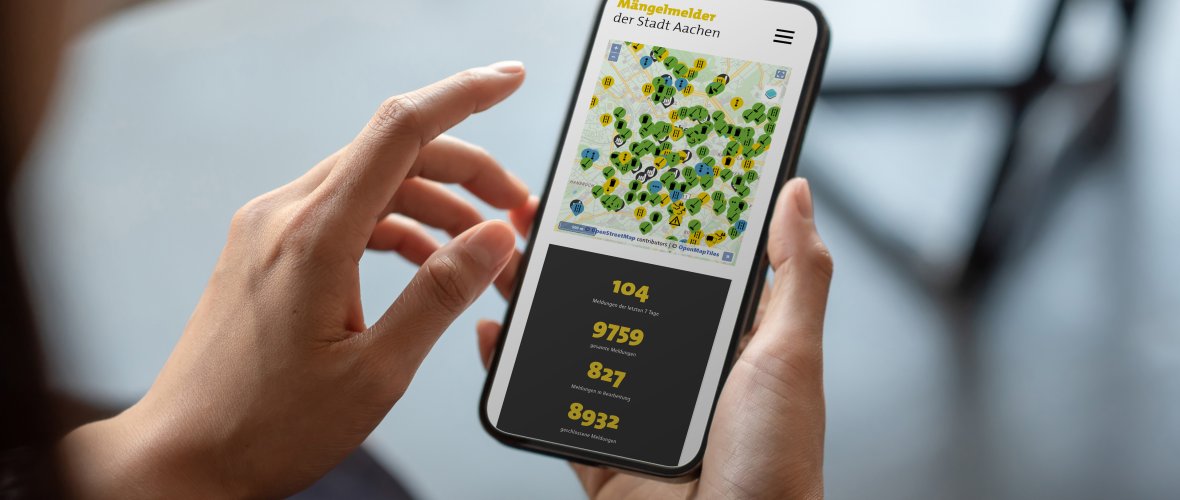 Une personne tient un smartphone dans la main et a ouvert le détecteur de défauts de la ville d'Aix-la-Chapelle.