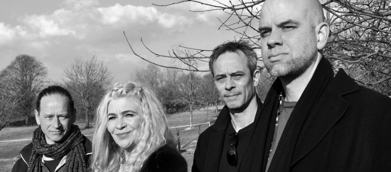 Image en noir et blanc du groupe Solid Ground. Les visages de trois hommes et d'une femme en gros plan.
