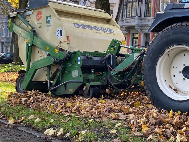 Un tracteur équipé d'un outil se déplace dans une prairie et ramasse les feuilles mortes.