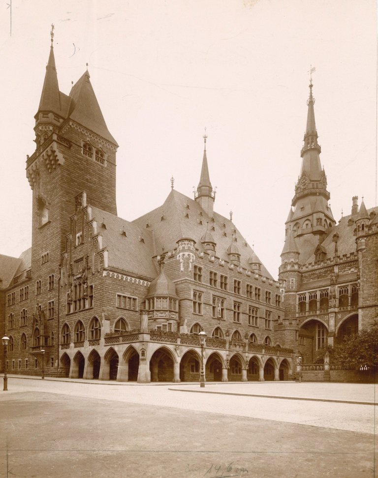 Photo historique de l'ancien bâtiment administratif du Katschhof avec une grande tour, de nombreuses petites tours et une colonnade. A droite, en coupe, l'hôtel de ville d'Aix-la-Chapelle.